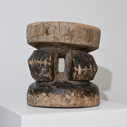 A hand carved indigenous West African dark brown wooden stool with a rounded top and faceted legs