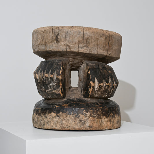 A hand carved indigenous West African dark brown wooden stool with a rounded top and faceted legs