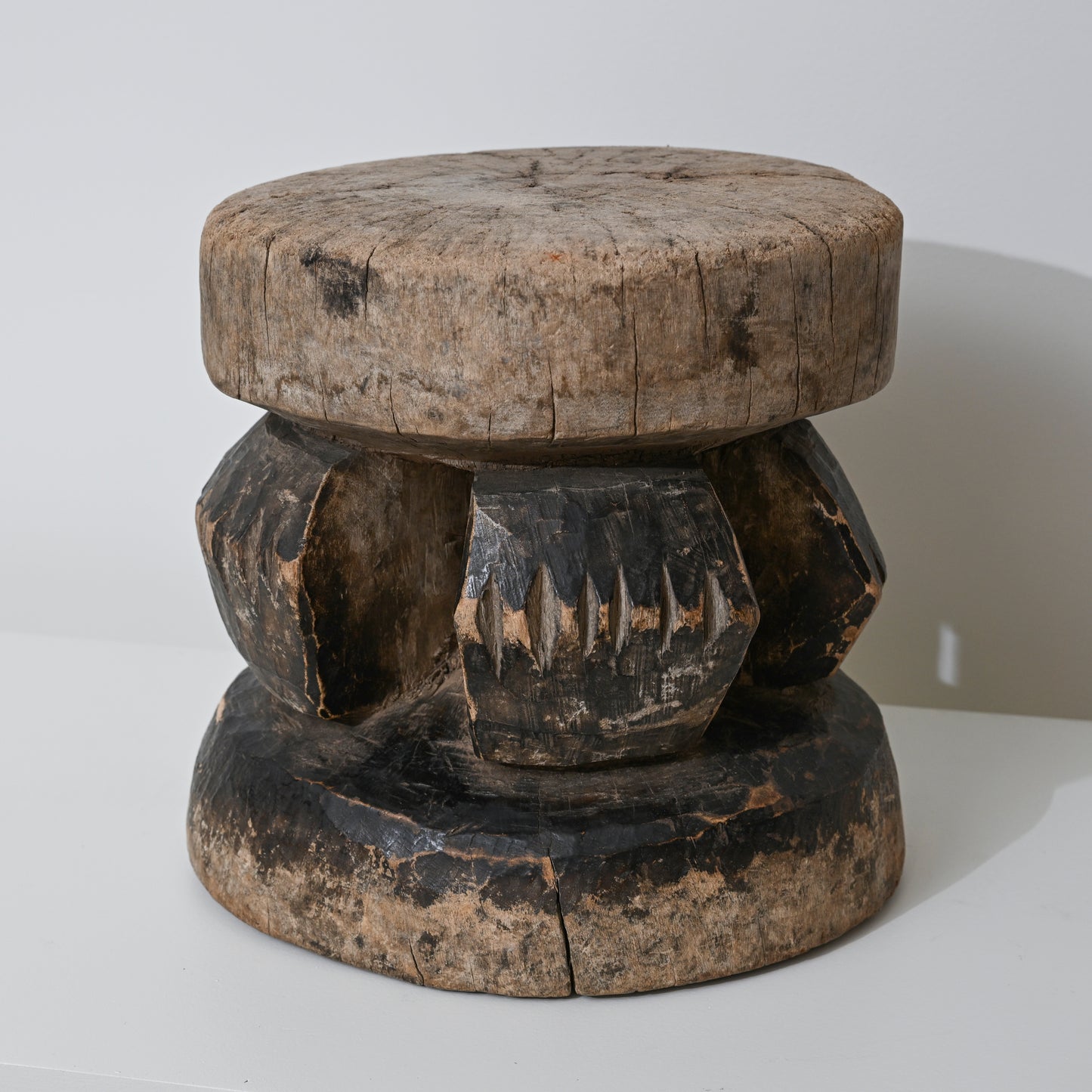 Hand carved indigenous West African wooden stool with weathered round top and dark carved geometric base