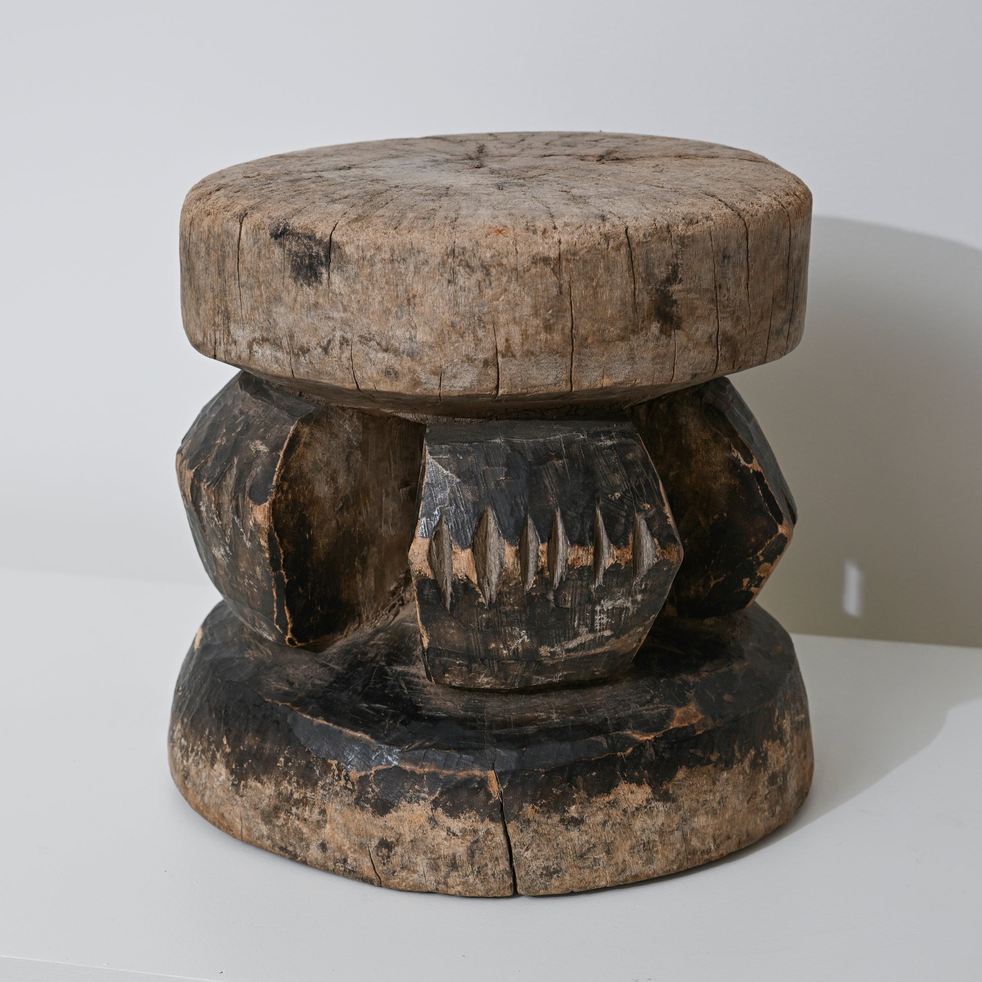 Hand carved indigenous West African wooden stool with weathered round top and dark carved geometric base