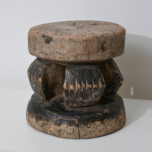 Hand carved indigenous West African wooden stool with weathered round top and dark carved geometric base