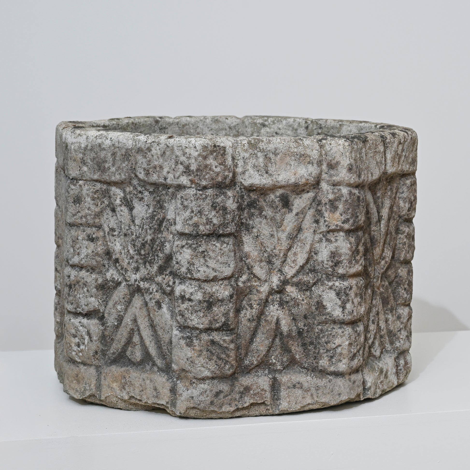 The 19th Century English Concrete Jardinere is a cylindrical, weathered stone planter featuring rough surfaces with repeating geometric and floral carvings, shown against a plain white background.