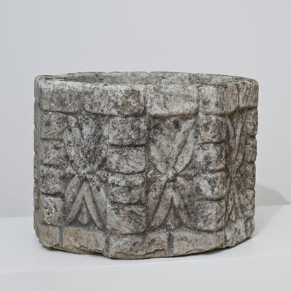The 19th Century English Concrete Jardinere is a cylindrical, weathered stone planter featuring rough surfaces with repeating geometric and floral carvings, shown against a plain white background.