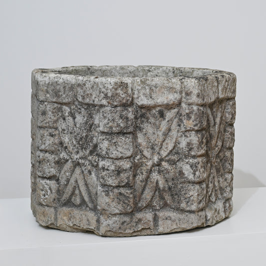 The 19th Century English Concrete Jardinere is a cylindrical, weathered stone planter featuring rough surfaces with repeating geometric and floral carvings, shown against a plain white background.