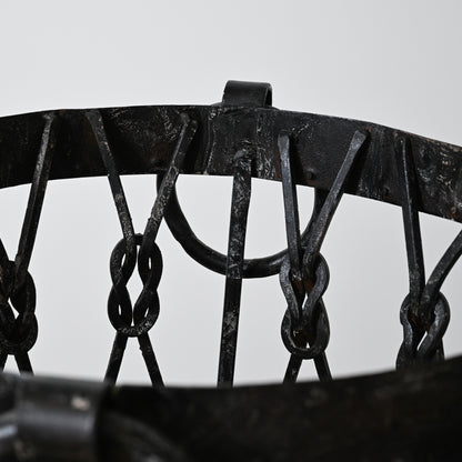 Black wrought iron wood holder basket with intricate chain links and rustic weathered finish for firewood storage