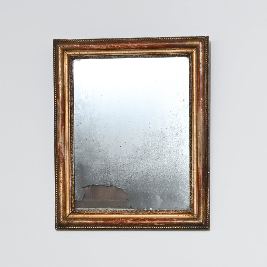 Early 19th Century Mercury Glass Mirror featuring a rectangular gilt wood frame. The antique glass is aged and distressed, with visible tarnish and wear—especially at the bottom edge—set against a plain, light-colored background.