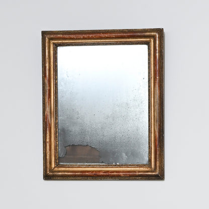 Early 19th Century Mercury Glass Mirror featuring a rectangular gilt wood frame. The antique glass is aged and distressed, with visible tarnish and wear—especially at the bottom edge—set against a plain, light-colored background.