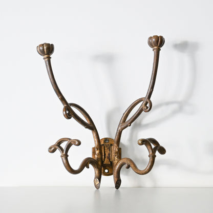 The Antique French Bronze Hook features four curved arms with floral-shaped ends, inspired by 1930s French decor. Its ornate, wall-mounted design casts elegant shadows on a white background.