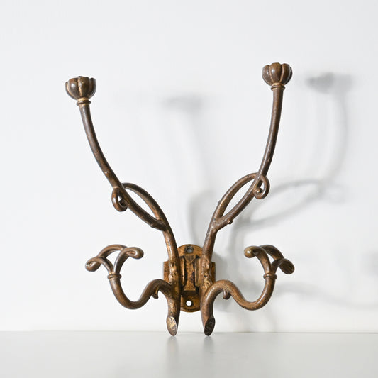 The Antique French Bronze Hook features four curved arms with floral-shaped ends, inspired by 1930s French decor. Its ornate, wall-mounted design casts elegant shadows on a white background.