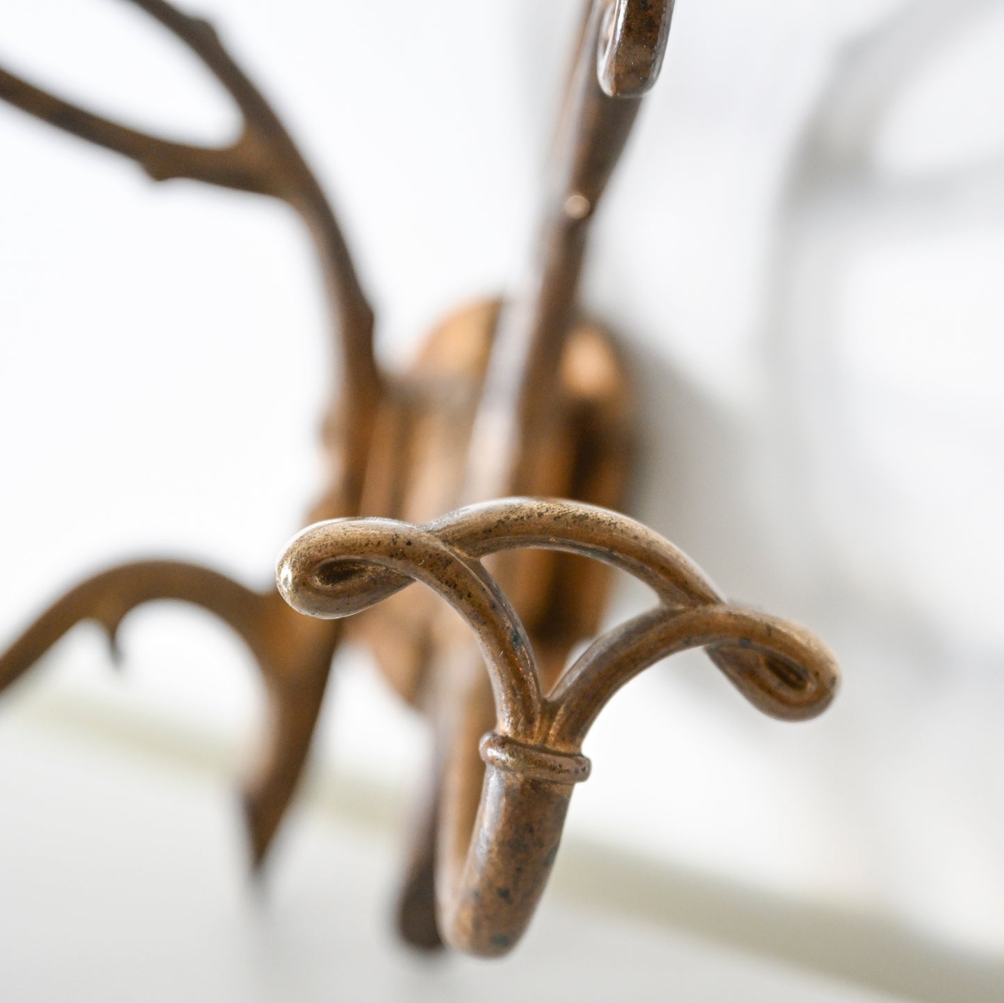 Close-up of the Antique French Bronze Hook featuring multiple curved arms, inspired by 1930s French decor, wall-mounted against a blurred white background.