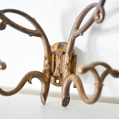 A close-up of the Antique French Bronze Hook with curved decorative arms and an aged rustic finish, inspired by 1930s French decor, mounted on a white wall.
