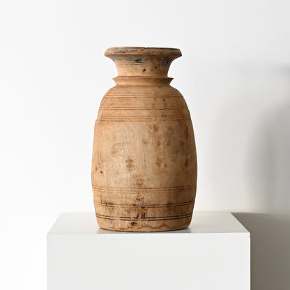 A rustic light brown wooden vase with subtle horizontal carvings and natural wood grain from primitive wood vessels