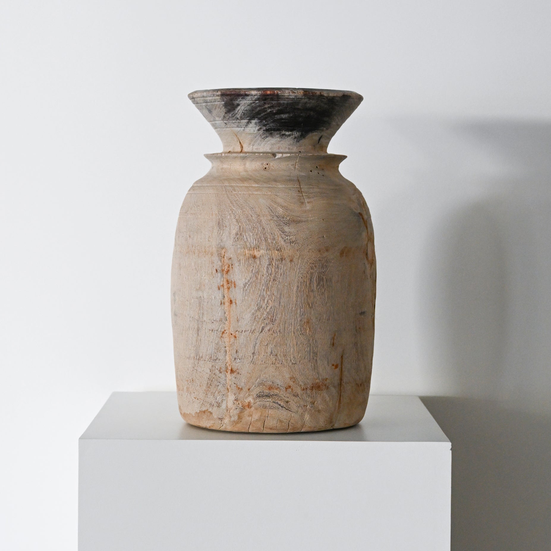 A rustic beige ceramic primitive wood vessel with a flared rim darkened top and subtle wood grain texture