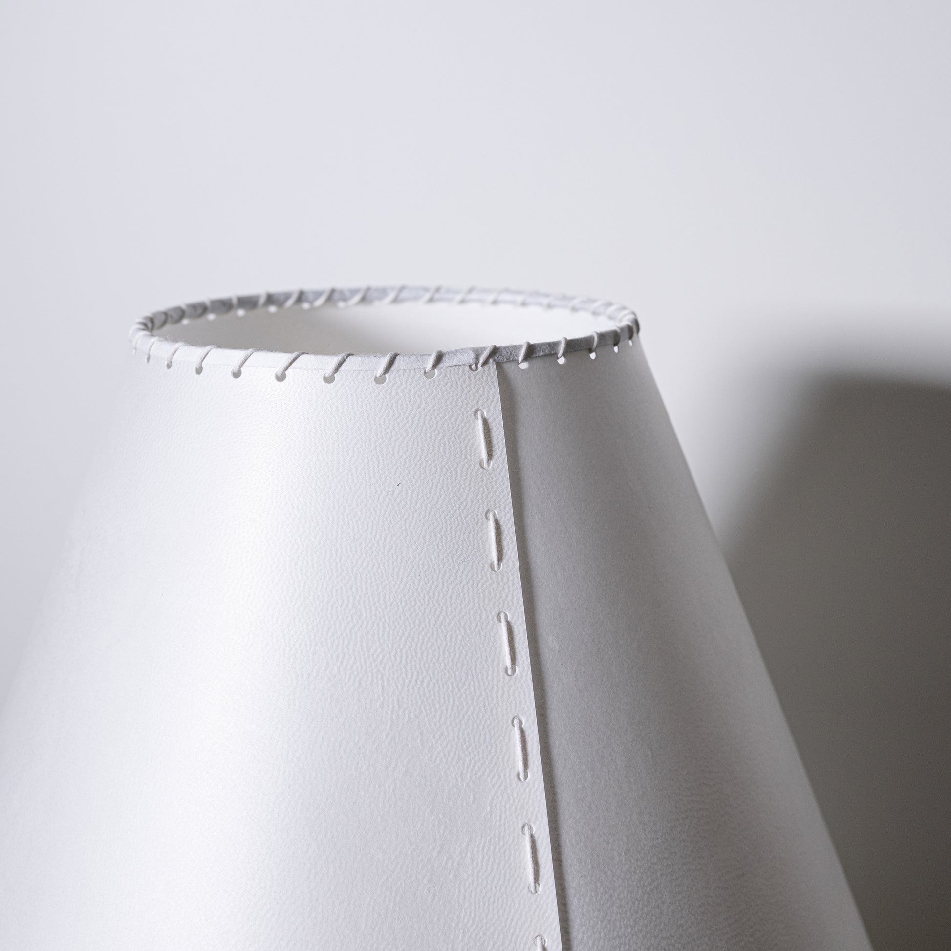 Brass and parchment table lamp with white conical lampshade featuring stitched edges and subtle texture