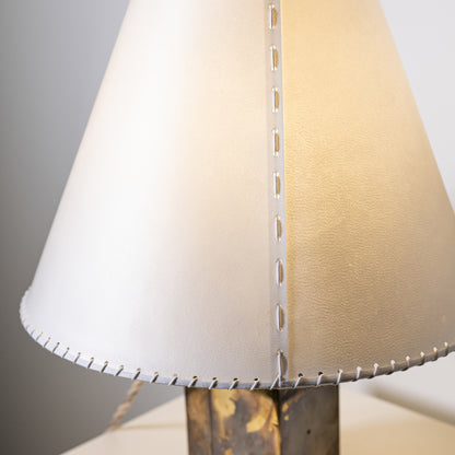 Cream-colored leather lampshade with silver stitching and metal fasteners on brass and parchment table lamp