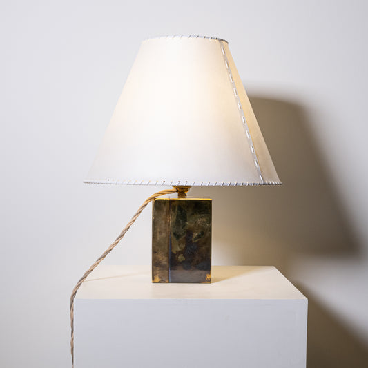 A sleek brass and parchment table lamp with a white fabric shade featuring subtle stitching along the edges