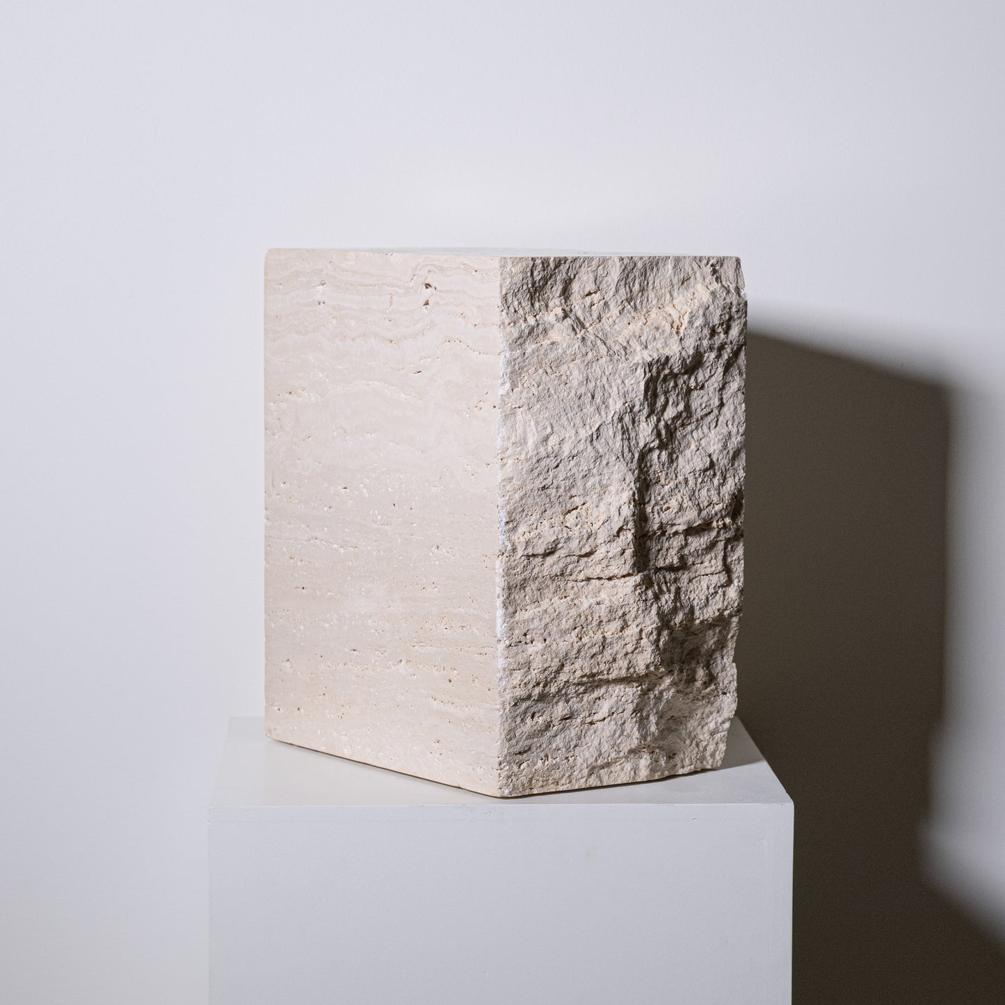Travertine block side table in beige stone with rough textured surface on one side and smooth finish on the other