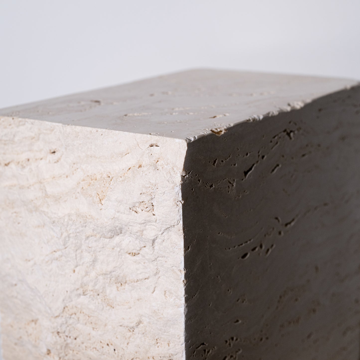 A minimalist travertine block side table with a textured light beige concrete top and dark gray contrasting side
