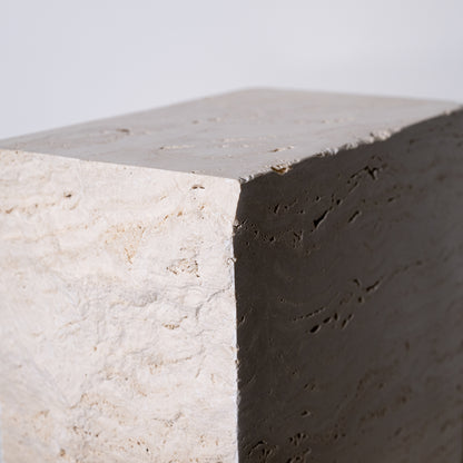 A minimalist travertine block side table with a textured light beige concrete top and dark gray contrasting side