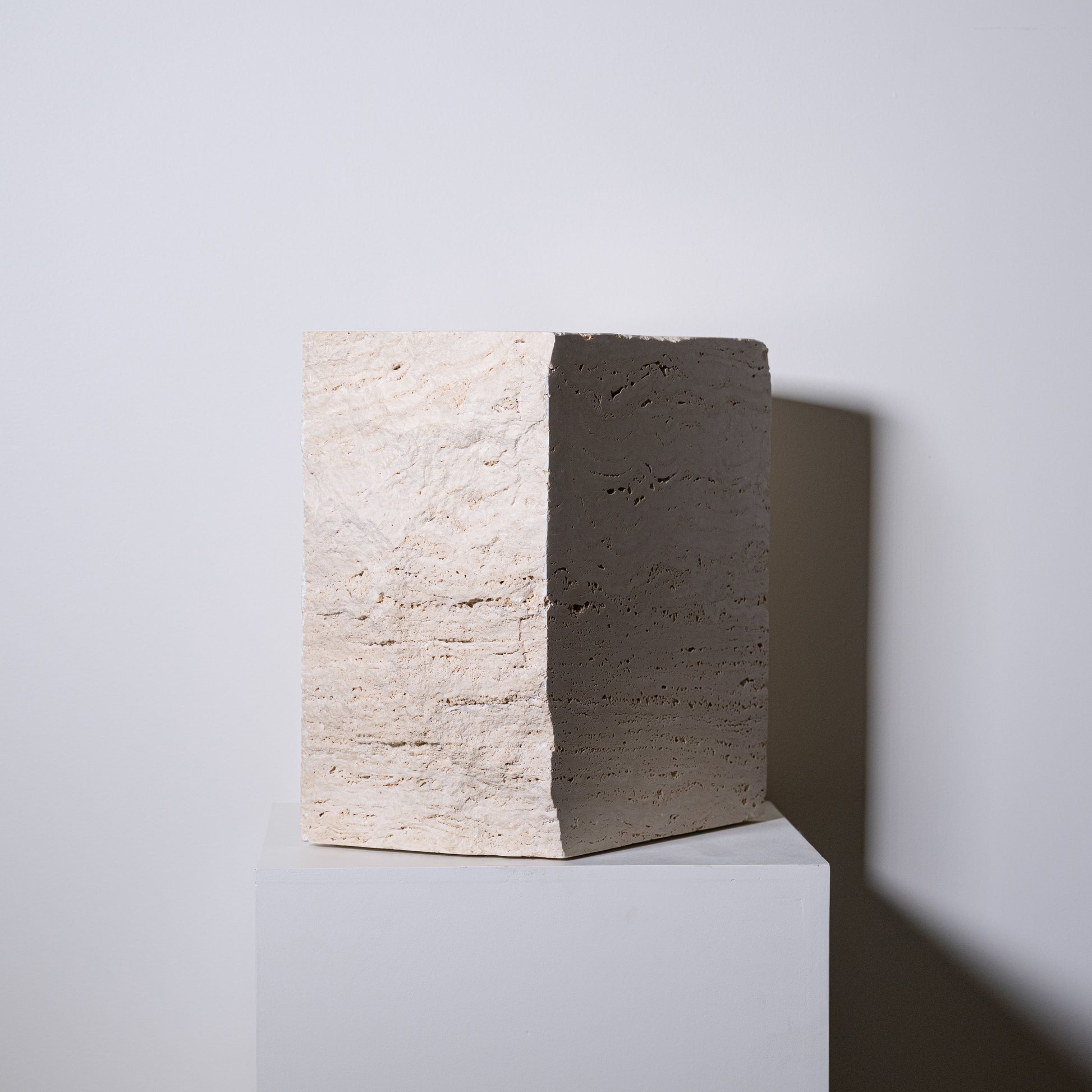 Minimalist travertine block side table with textured off-white concrete surface and smooth dark gray face