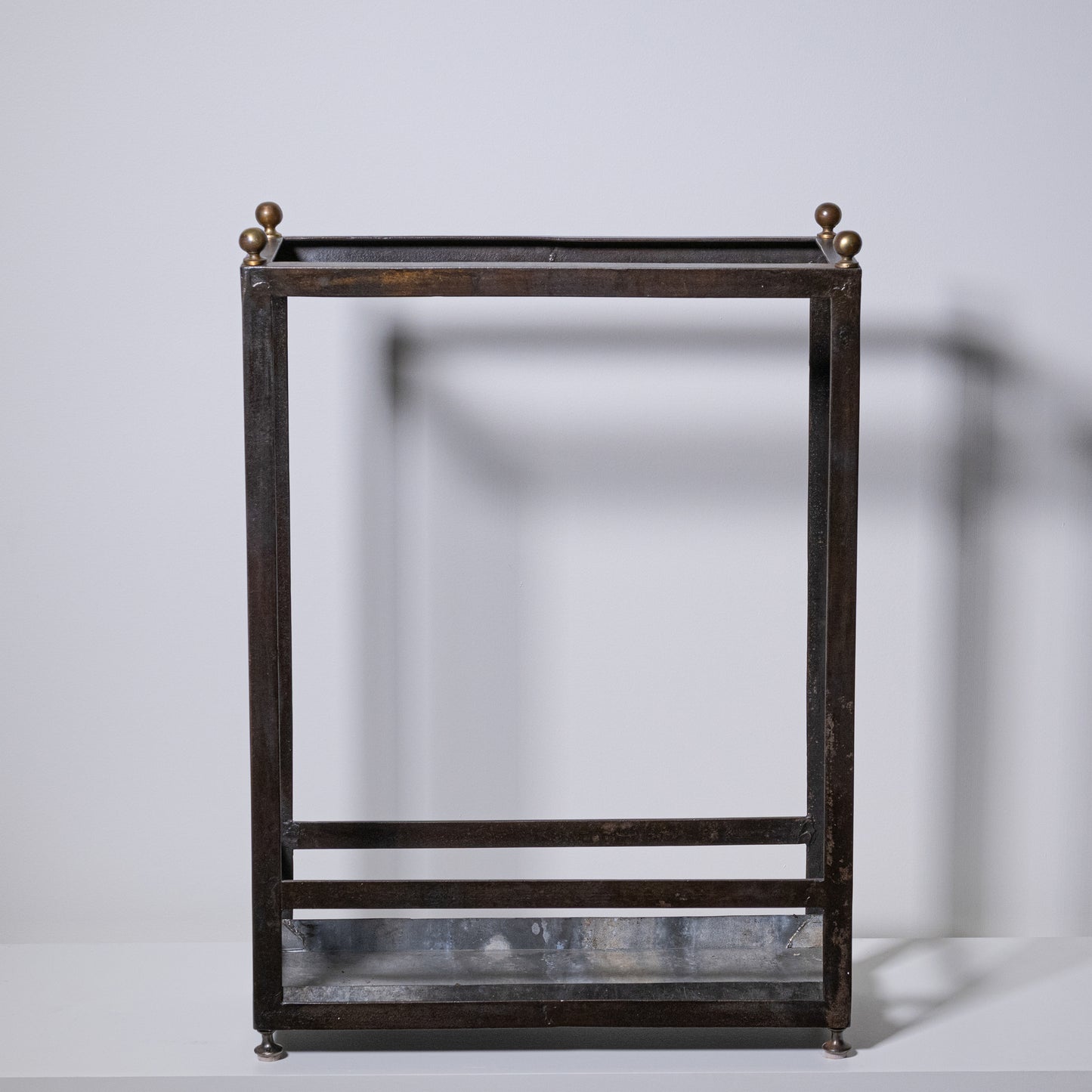 Antique umbrella stand with dark bronze metal body, brass finials, and glass base for elegant storage