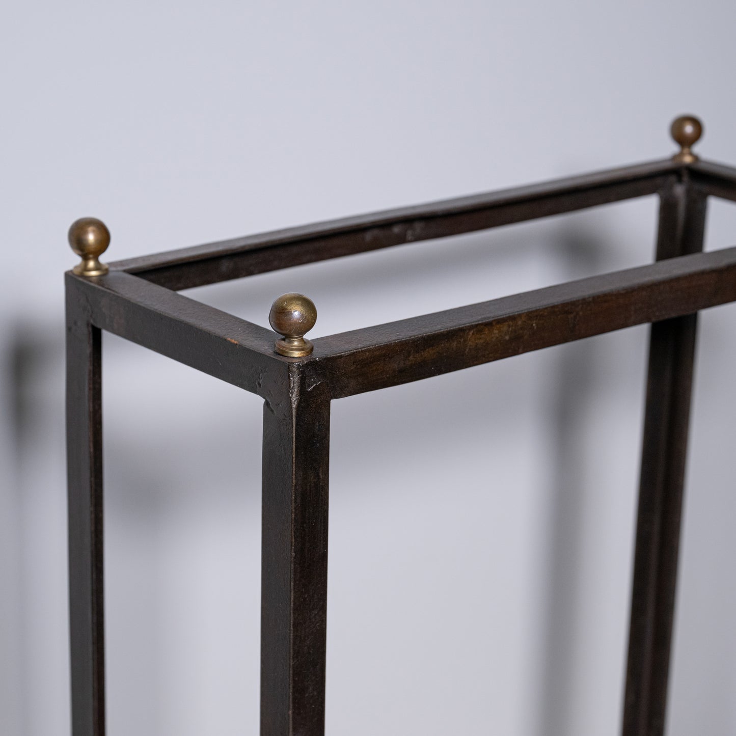 Antique umbrella stand in dark bronze metal with brass spherical finials at each corner for elegant storage
