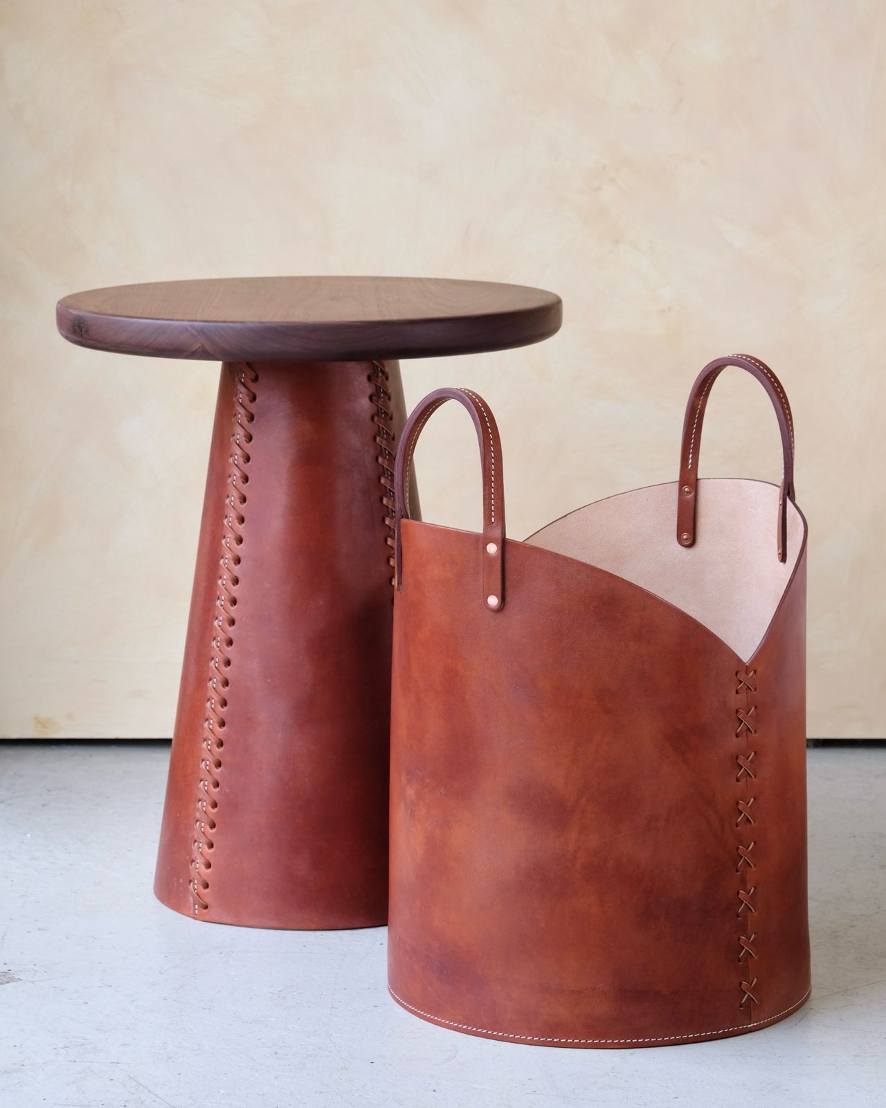 Brown leather log basket with cylindrical shape stitched handles and x-shaped side stitching for firewood storage