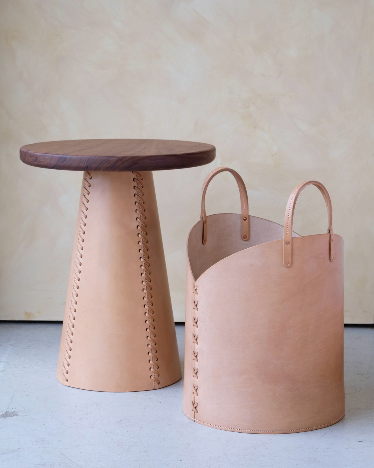 Tan leather log basket with curved handles and decorative stitching designed as a bucket style container