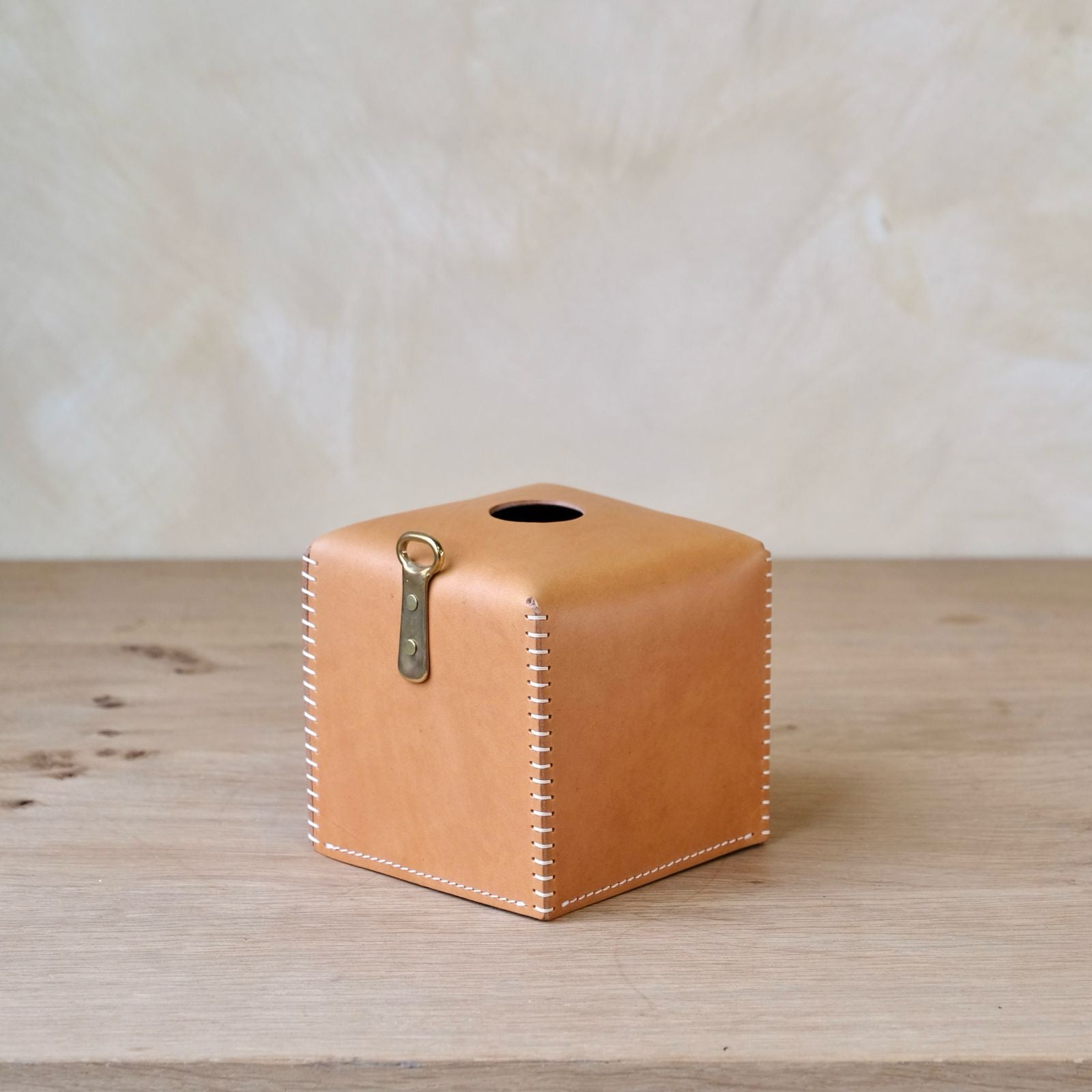 Tan leather tissue box cover with white stitching and brass clasp for stylish and durable tissue storage
