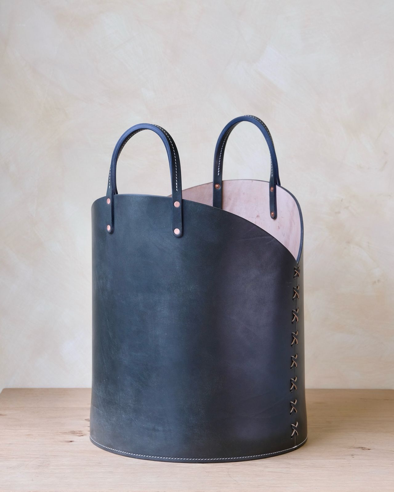 Dark blue leather log basket with light pink interior and decorative stitching for firewood storage