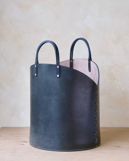 Dark blue leather log basket with light pink interior and decorative stitching for firewood storage