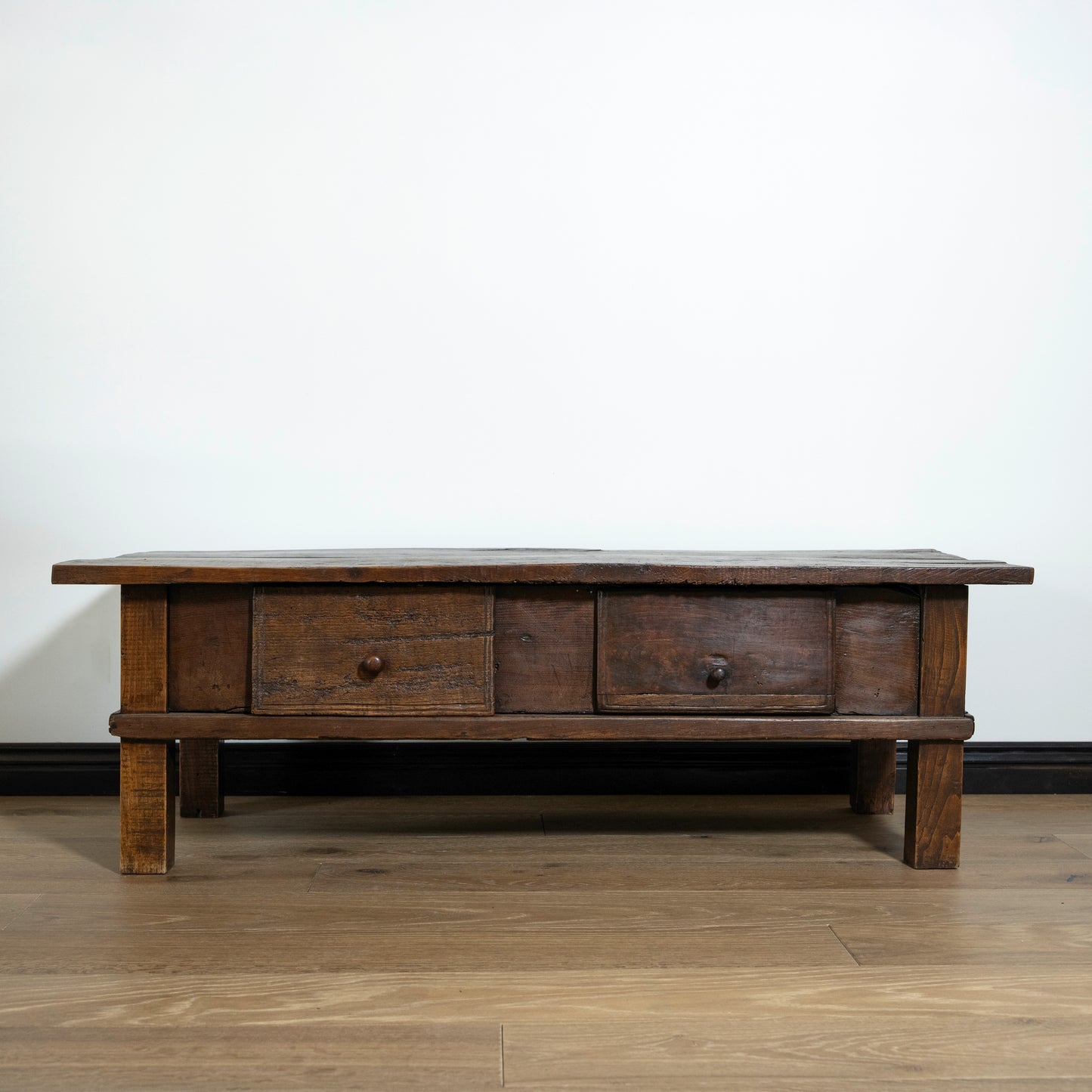 Wooden coffee table with three drawers on a wooden floor against a white wall