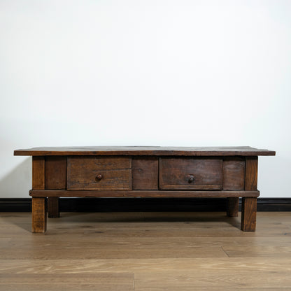 Wooden coffee table with three drawers on a wooden floor against a white wall