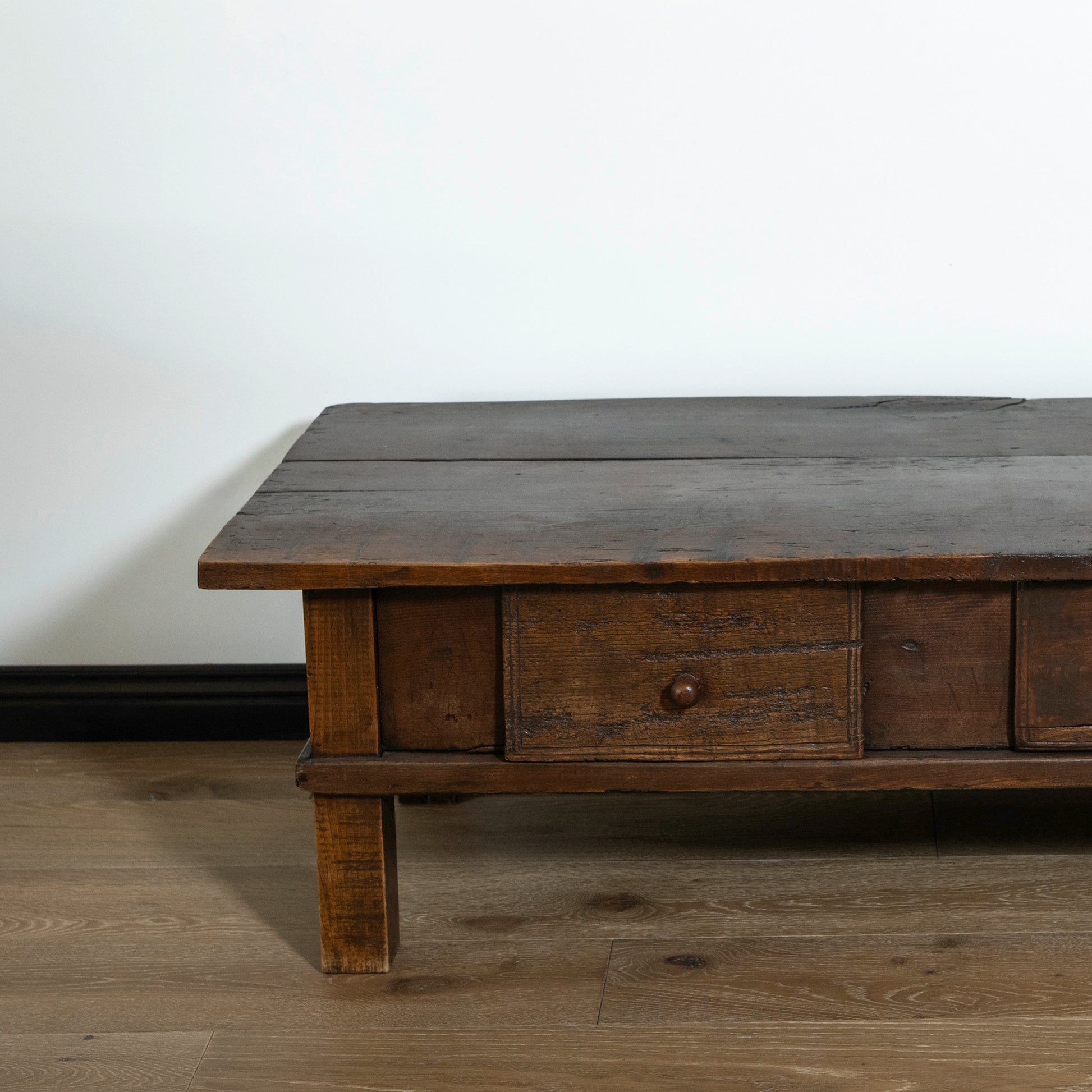 Wooden coffee table with a single drawer on a wooden floor against a white wall.