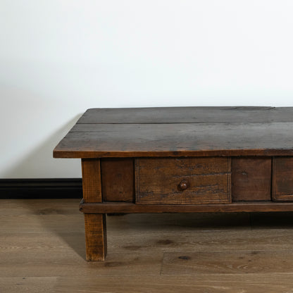 Wooden coffee table with a single drawer on a wooden floor against a white wall.