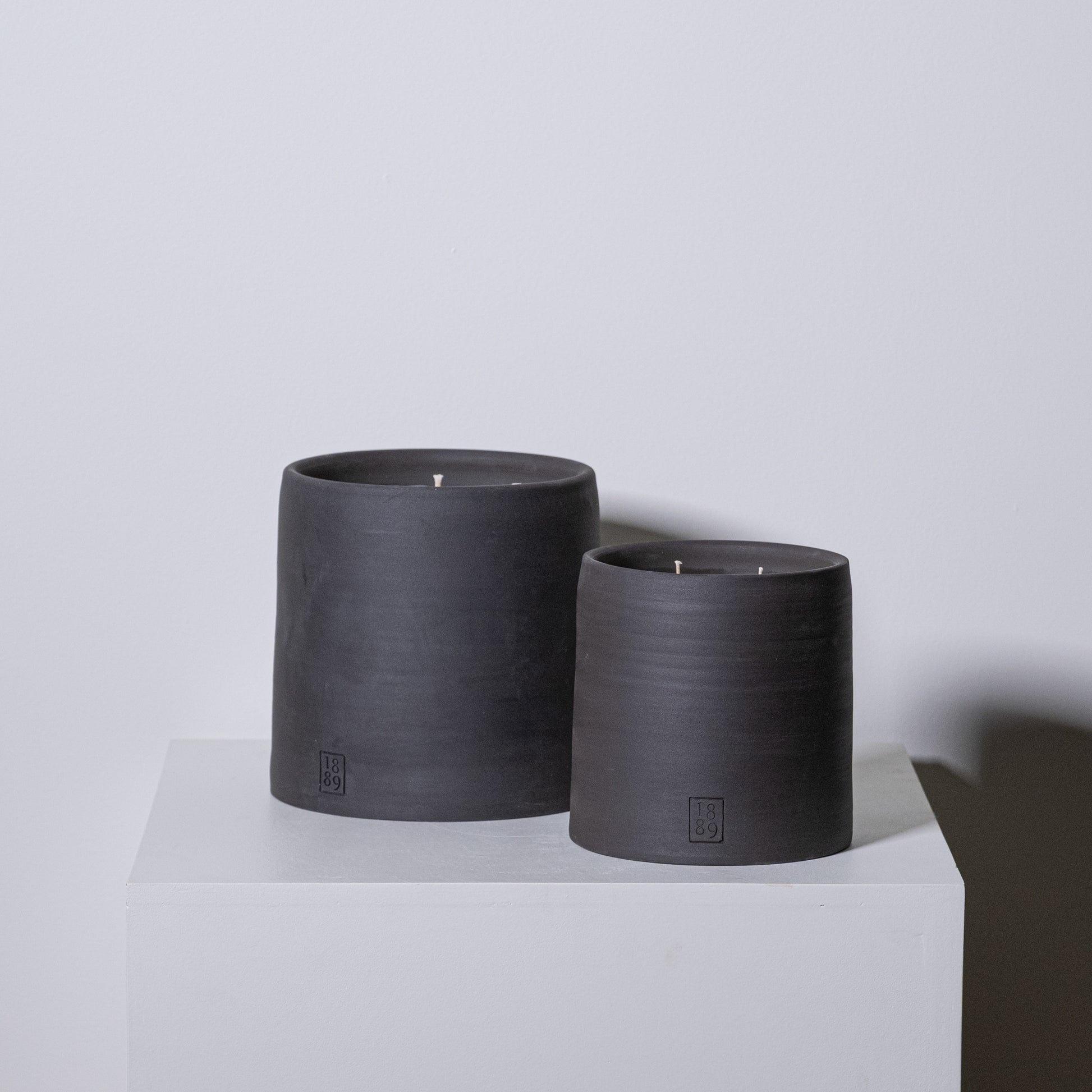Two matte black ceramic candle holders with single wicks and embossed branding for candle trapper use