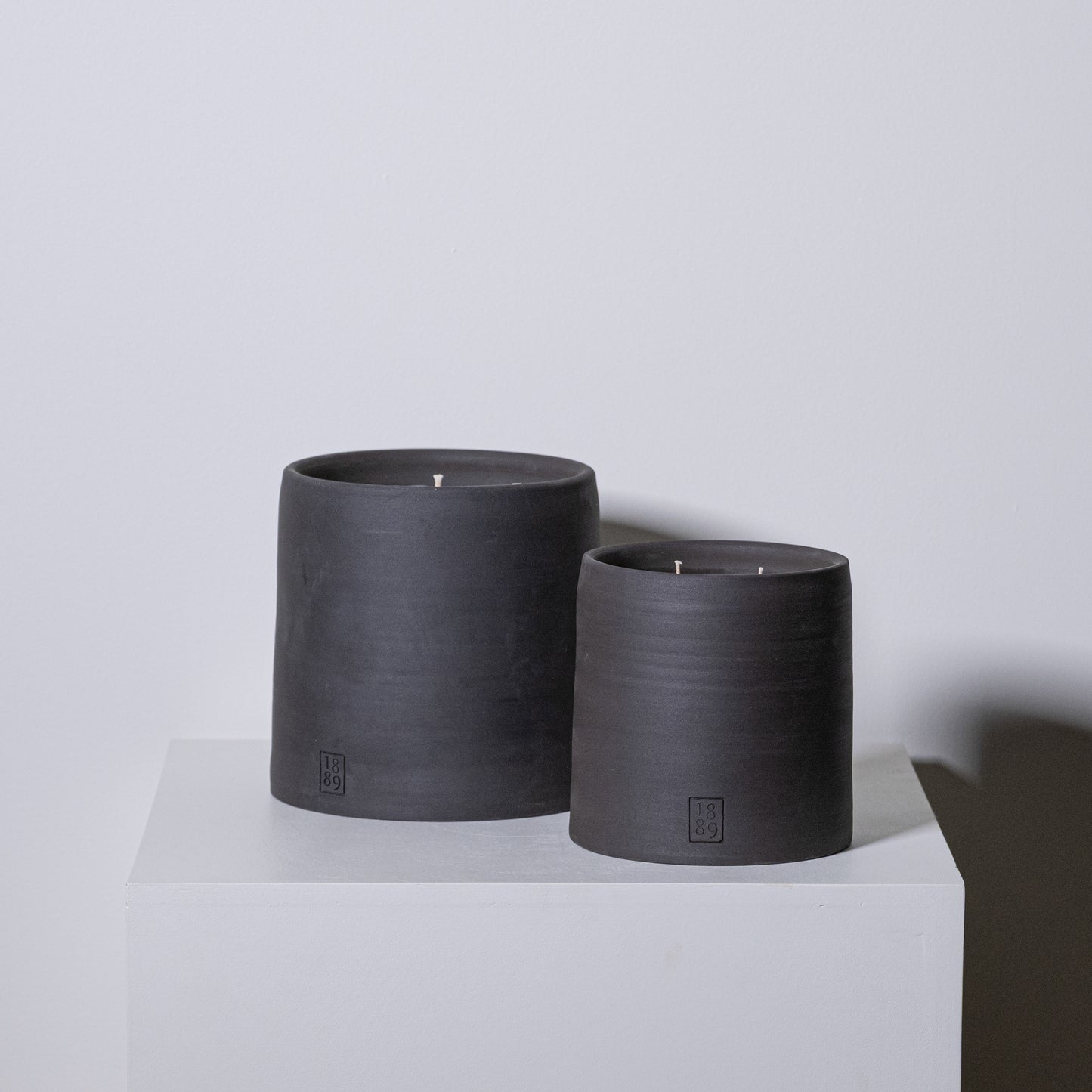Two matte black ceramic candle holders with single wicks and embossed branding from candle toscana collection