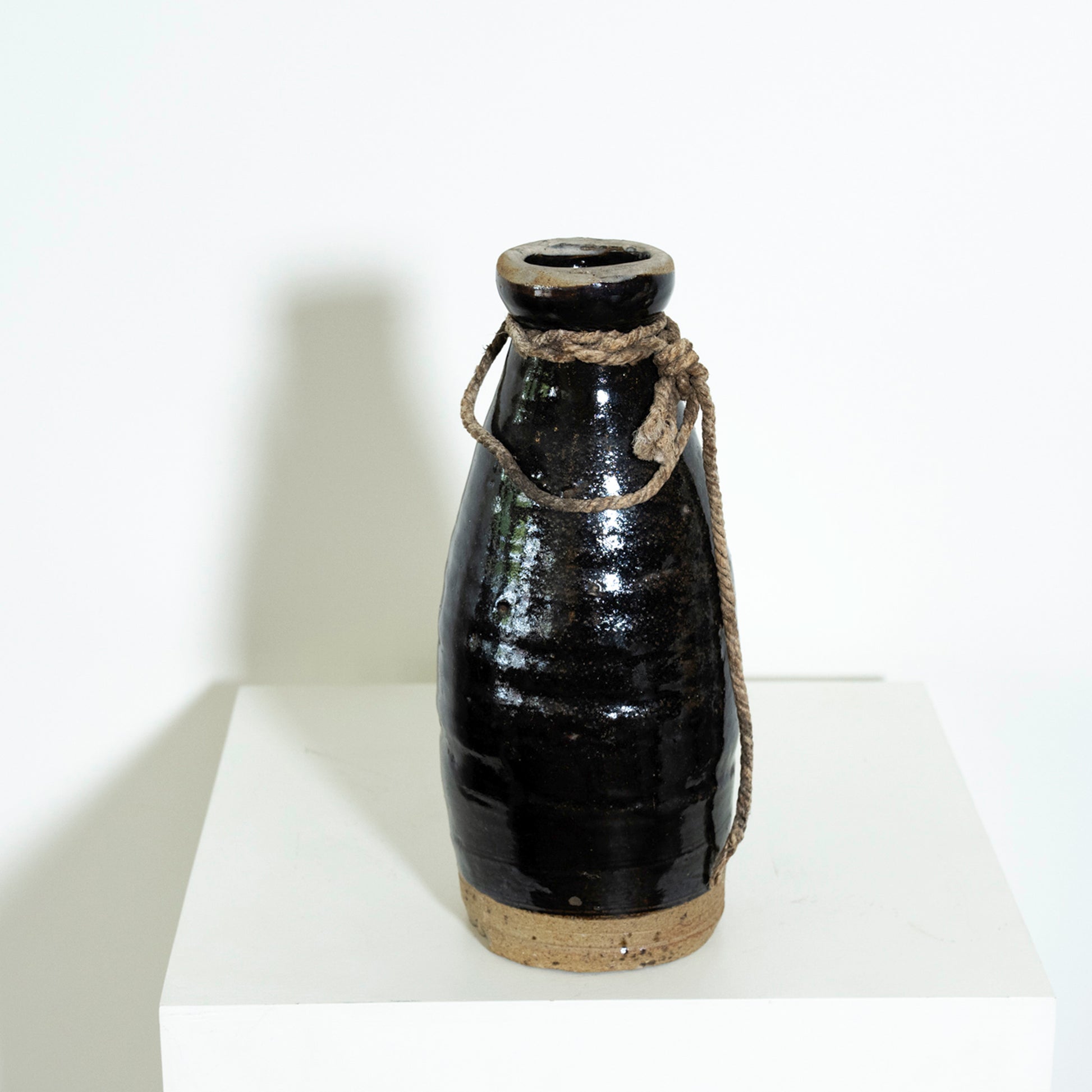 Black ceramic bottle with a rope handle on a white pedestal