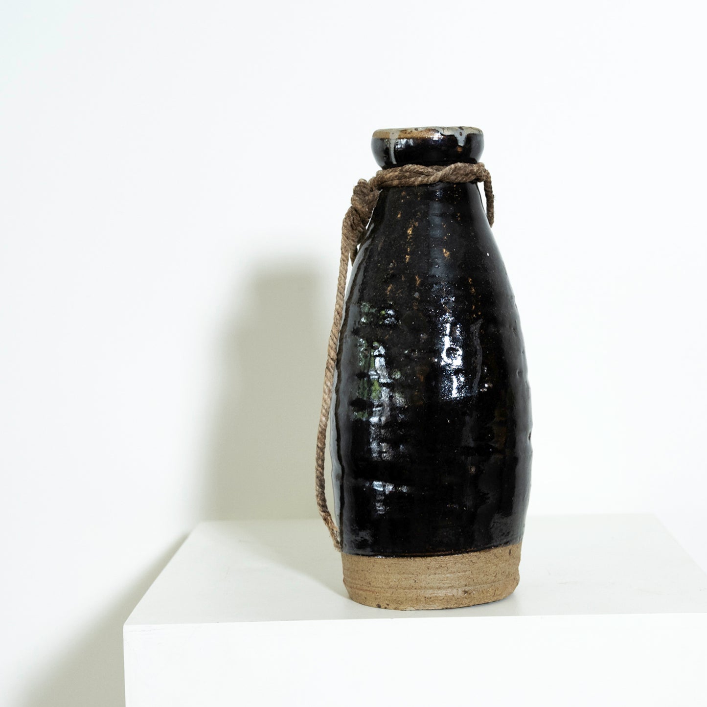 Black ceramic bottle with a rope handle on a white background