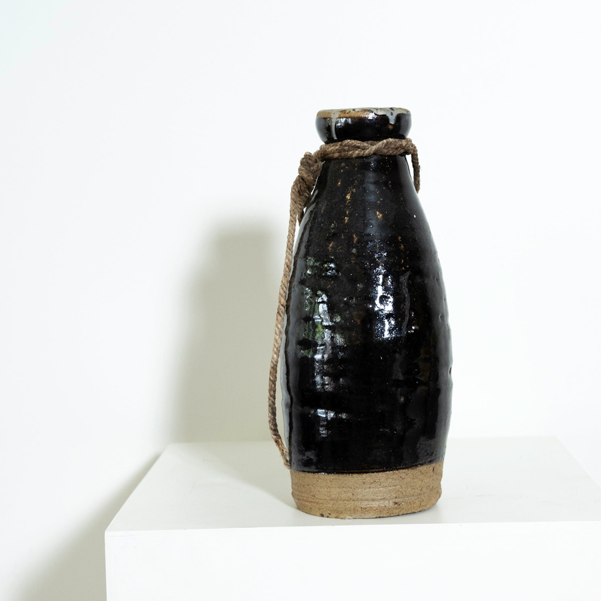 Black ceramic bottle with a rope handle on a white background