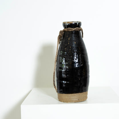 Black ceramic bottle with a rope handle on a white background