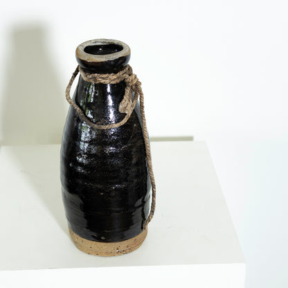 Black ceramic bottle with rope handle on a white surface
