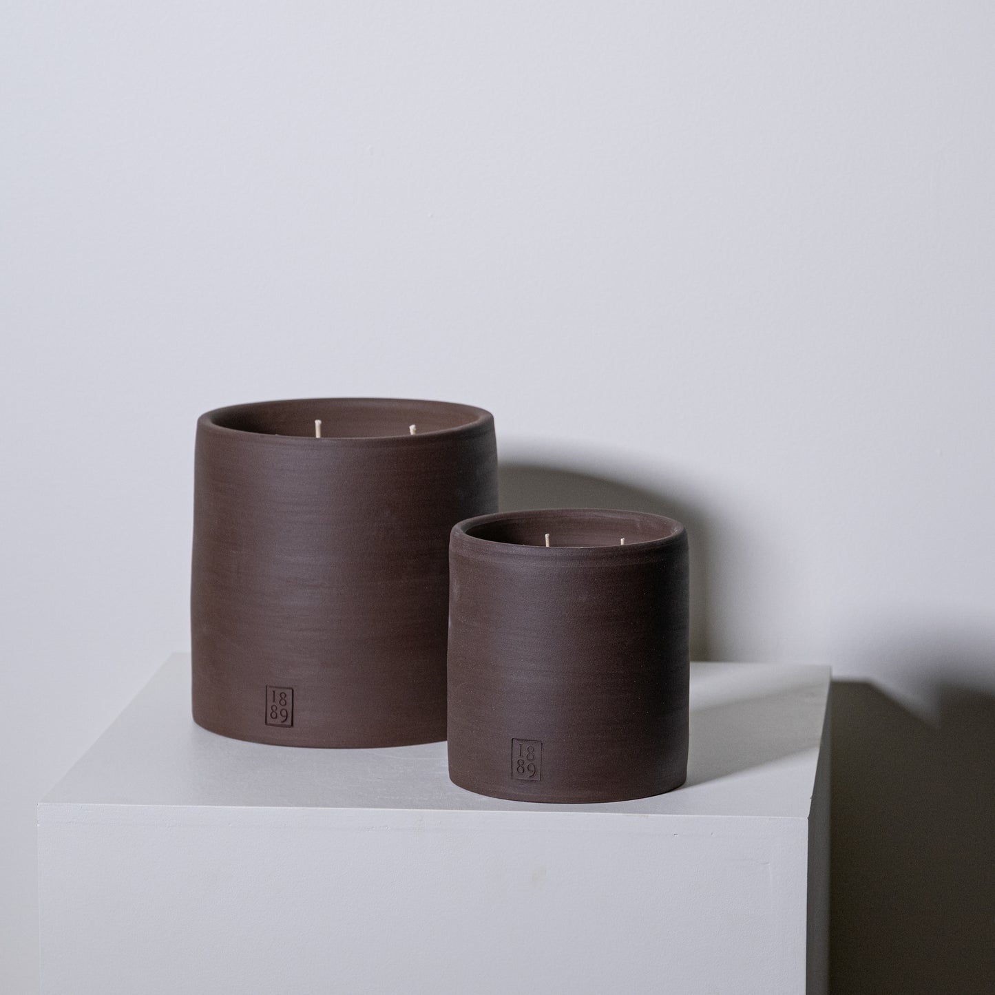 Two matte brown ceramic candle holders with three wicks each and a small embossed logo for toscana candles