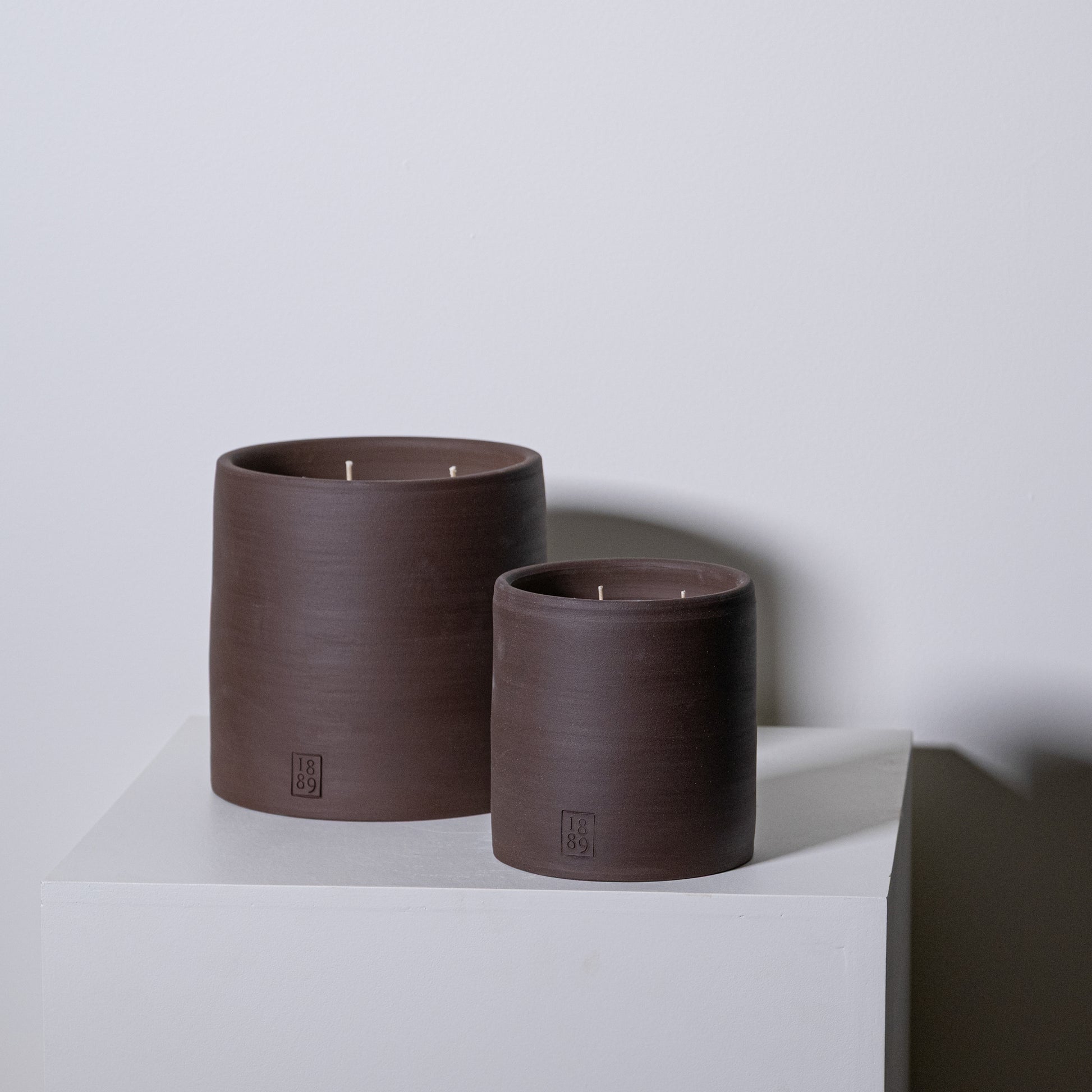 Two matte brown ceramic candle holders with three wicks each and a small embossed logo for toscana candles