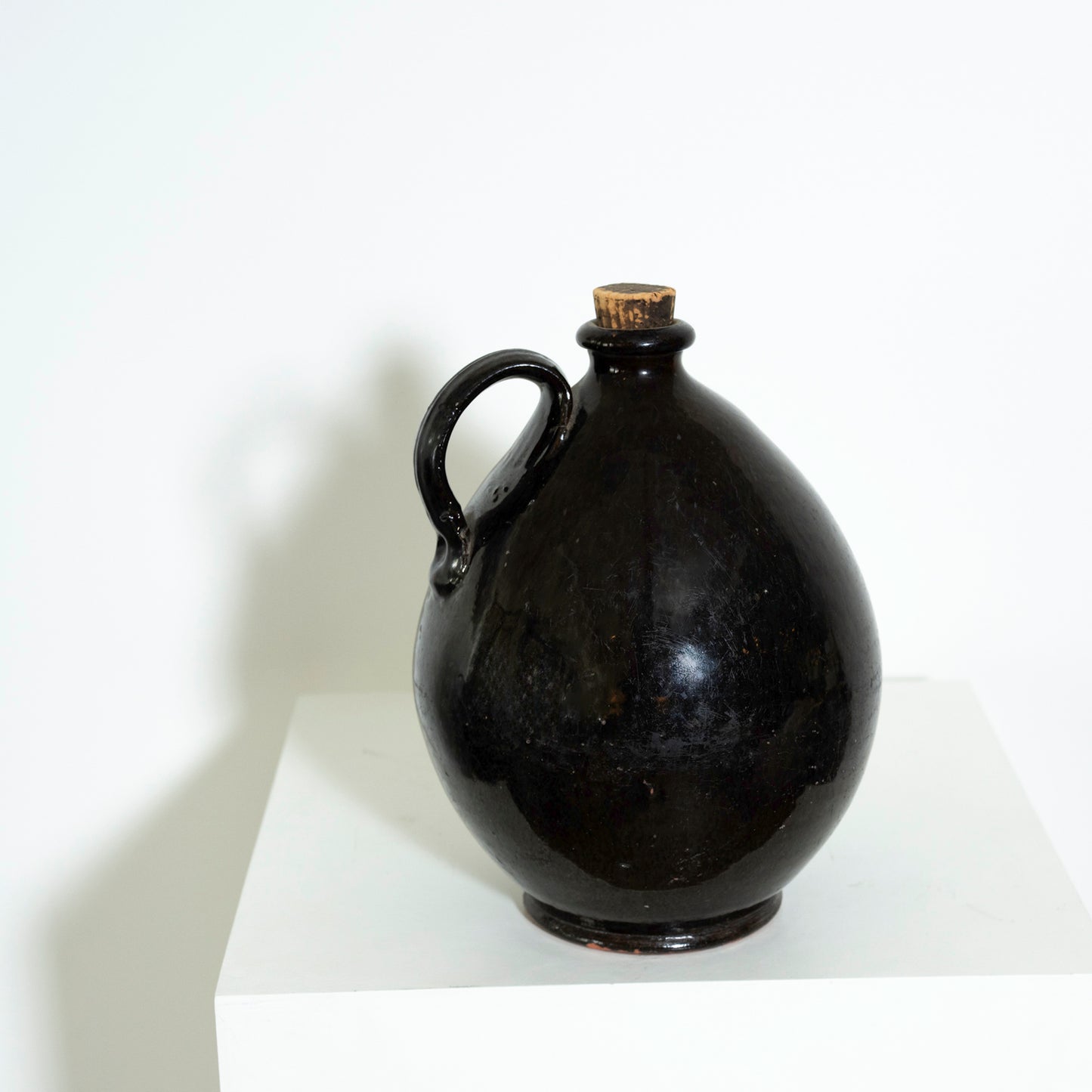 Black ceramic jug with a cork stopper on a white surface