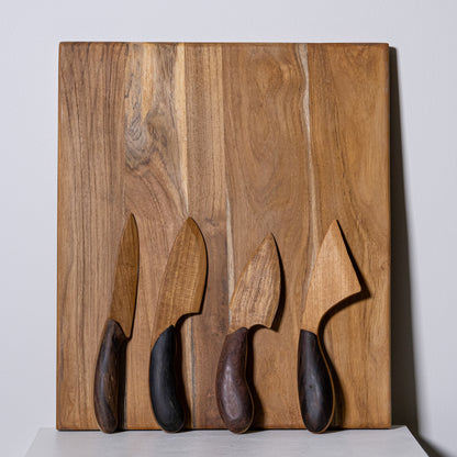 Set of four teak and sono knives with wooden handles and dark ergonomic grips on a rustic wood cutting board