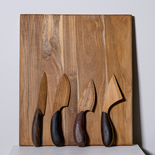 Set of four wooden-handled knives with dark ergonomic grips on a rustic wood cutting board for charcuterie use
