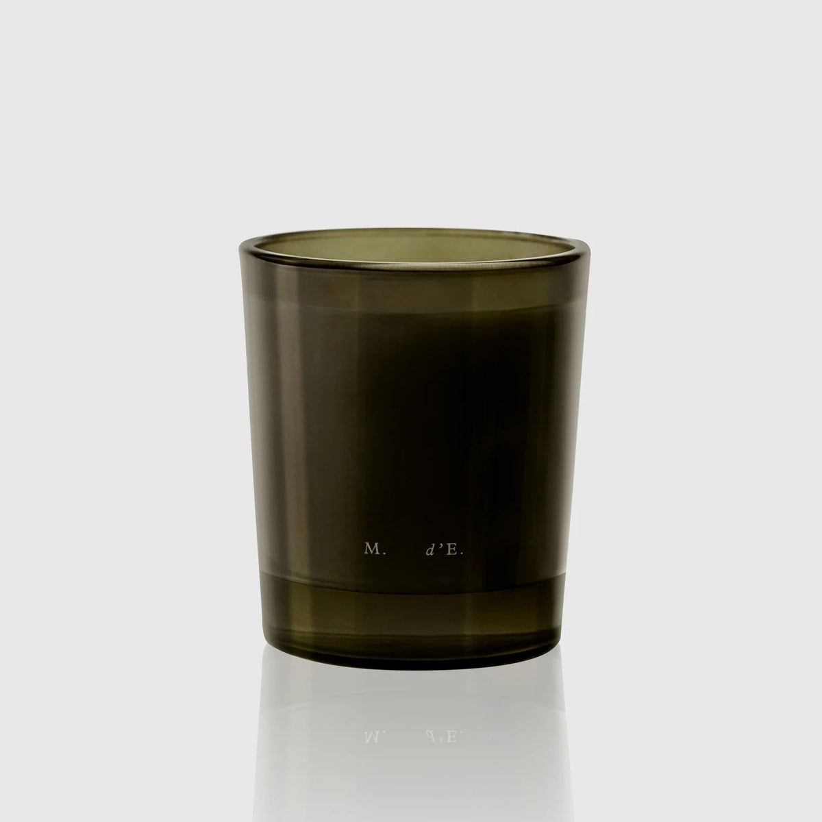 An olive green translucent glass candle holder with a small white printed logo, shown on a light gray reflective surface.