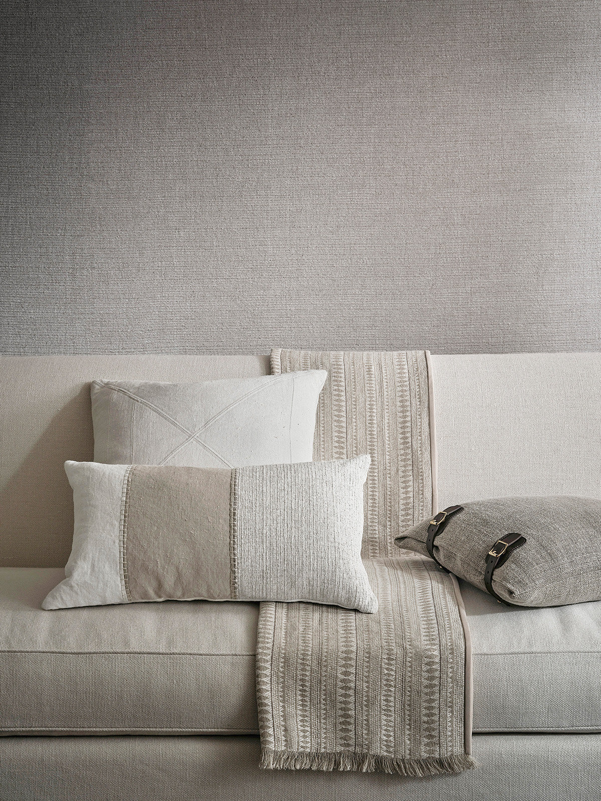 Beige woven linen throw blanket with fringe draped over sofa complementing painted linen panel pillow