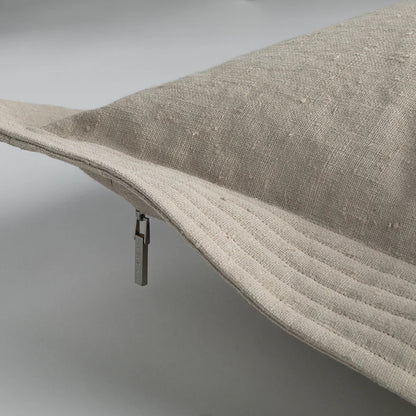 Beige linen bucket hat with ribbed brim and metallic zipper pull shown next to quilted edge pillow cement color